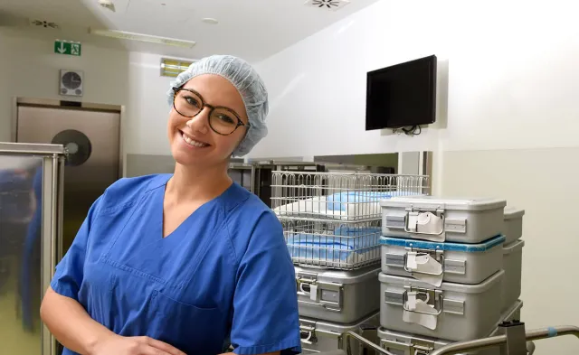 Sterile processing technician in lab wearing PPE posing and smiling for photo