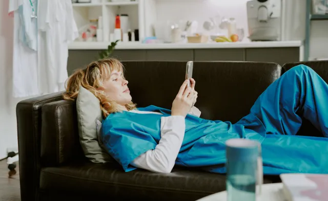 Young Caucasian nurse using smartphone while lying on black leather sofa in on call room