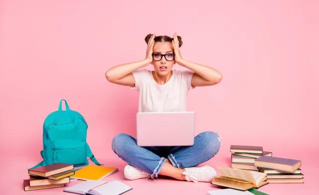Full legs, body, size portrait of confused girl in white T-shirt and blue jeans sitting on floor with laptop on knees isolated on bright pink background.