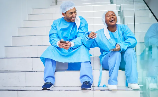 urgeon, conversation and laughing on hospital stairs with phone and funny meme. Healthcare, medical and doctor team relax with comic and conversation together with mobile and social networking