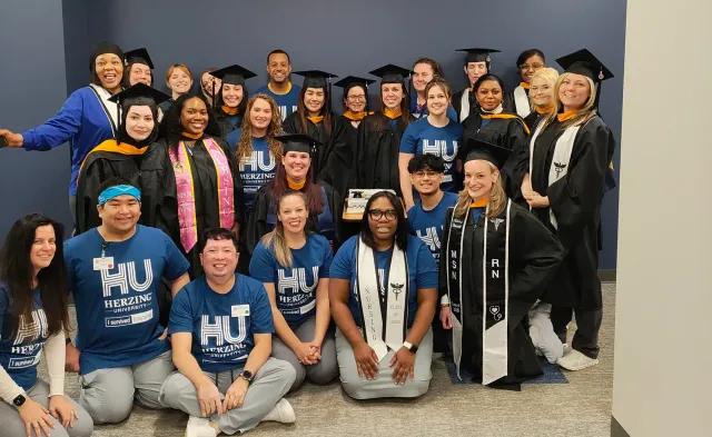 Group of Herzing University online nursing students posed for photo, some wearing a cap and gown after graduation