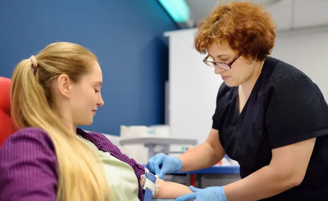 Healthcare worker drawing blood from a seated patient in a clinical setting
