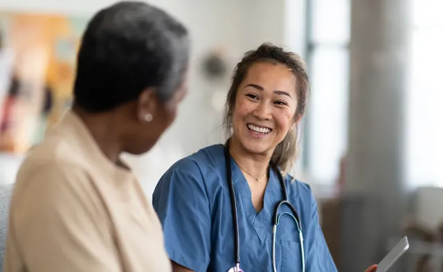 	Nurse in blue scrubs with a stethoscope smiles warmly while talking with a patient