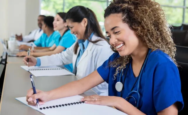 Beautiful female medical or nursing school student smiles as she takes notes during class.