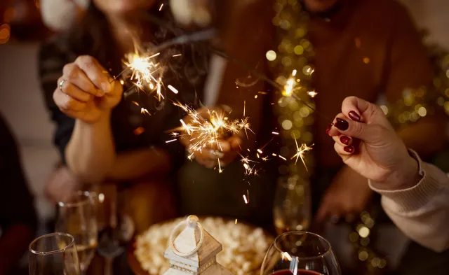 Close up of unrecognizable friends having fun with sparklers while celebrating Christmas at home.