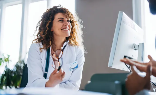 A smiling nurse in a white coat speaks with a patient during a consultation in a bright medical office.