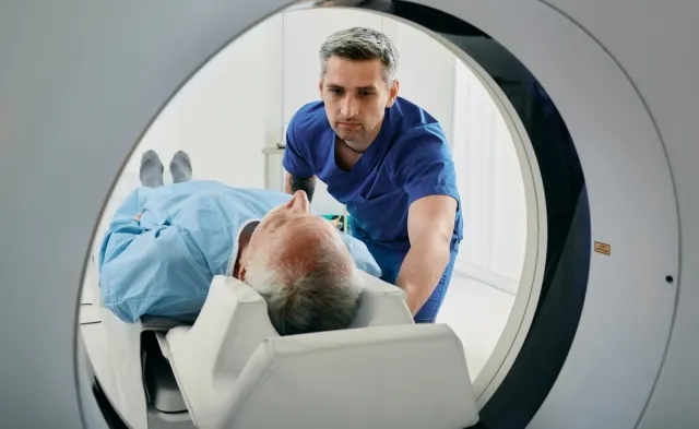 Radiologic technologist positions an older patient on the table of a CT scanner, preparing them for a medical imaging exam.