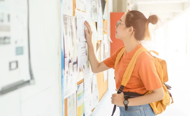 Unemployed young university woman looking for work or job after graduation at the post board