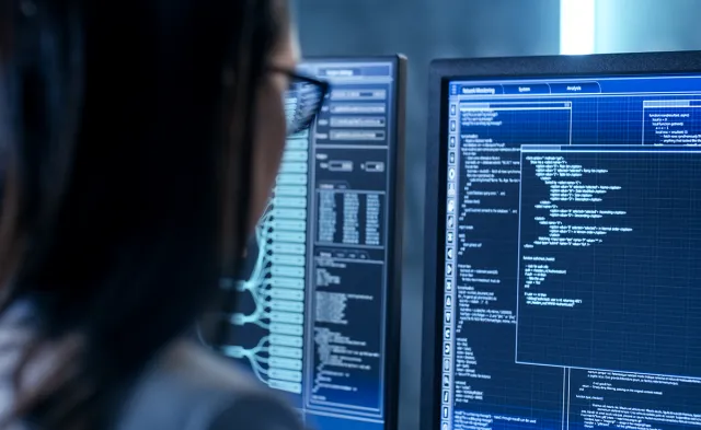 Woman seated at desk in front of computer doing programming