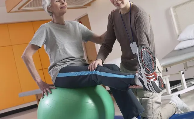 Physical therapist assistant providing PTA services for patient stretching on exercise ball