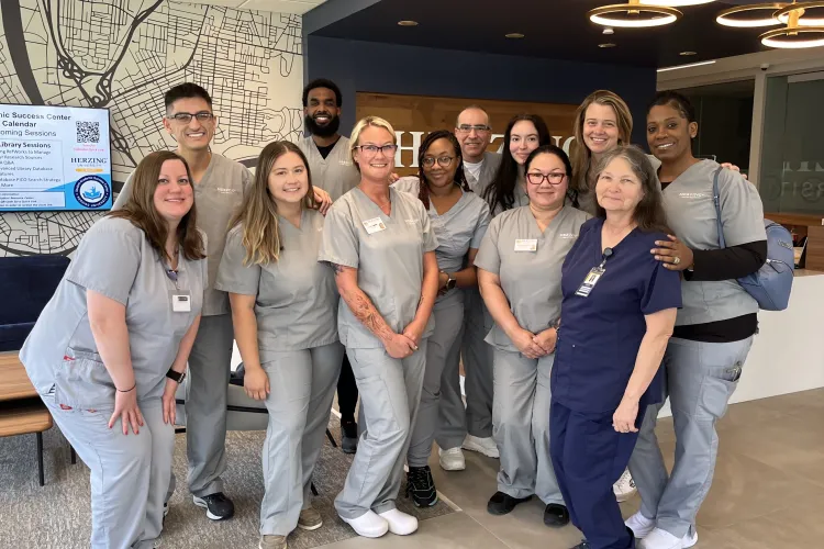 Group of Herzing University nursing students in gray scrubs smiling for photo during simulation lab.