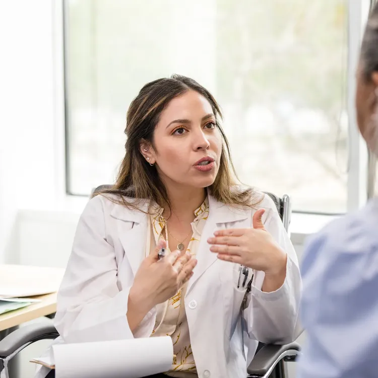 A nurse practitioner with holistic nursing certification in a white lab coat speaks with a patient during a consultation in a bright exam room.