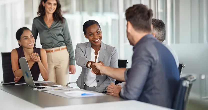 Human resources professional shaking hands with a candidate during a job interview in a modern office setting.