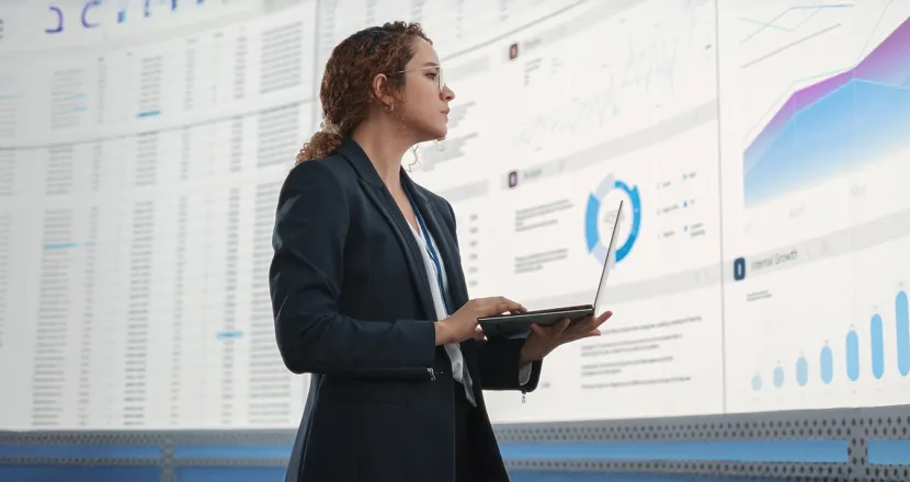 Professional analyzing data visualizations on a large screen while using a laptop.