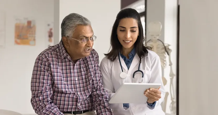 Older patient smiling while a nurse practitioner student reviews health information with him on a tablet