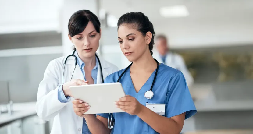Healthcare professionals review information together on a tablet, with one clinician pointing to the screen as the other reads.