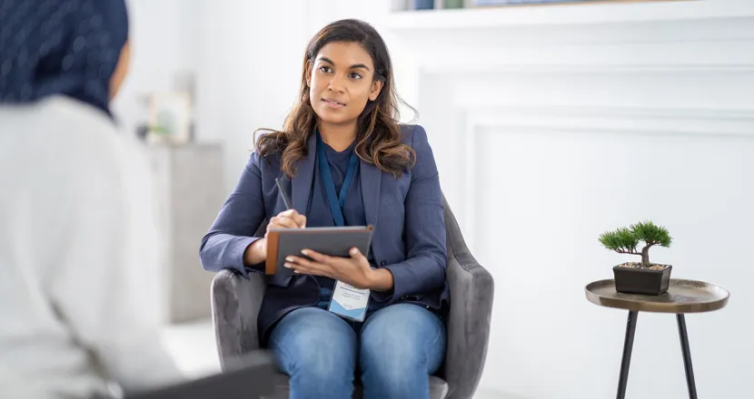 Counselor takes notes on a tablet while listening to a client in a private office.