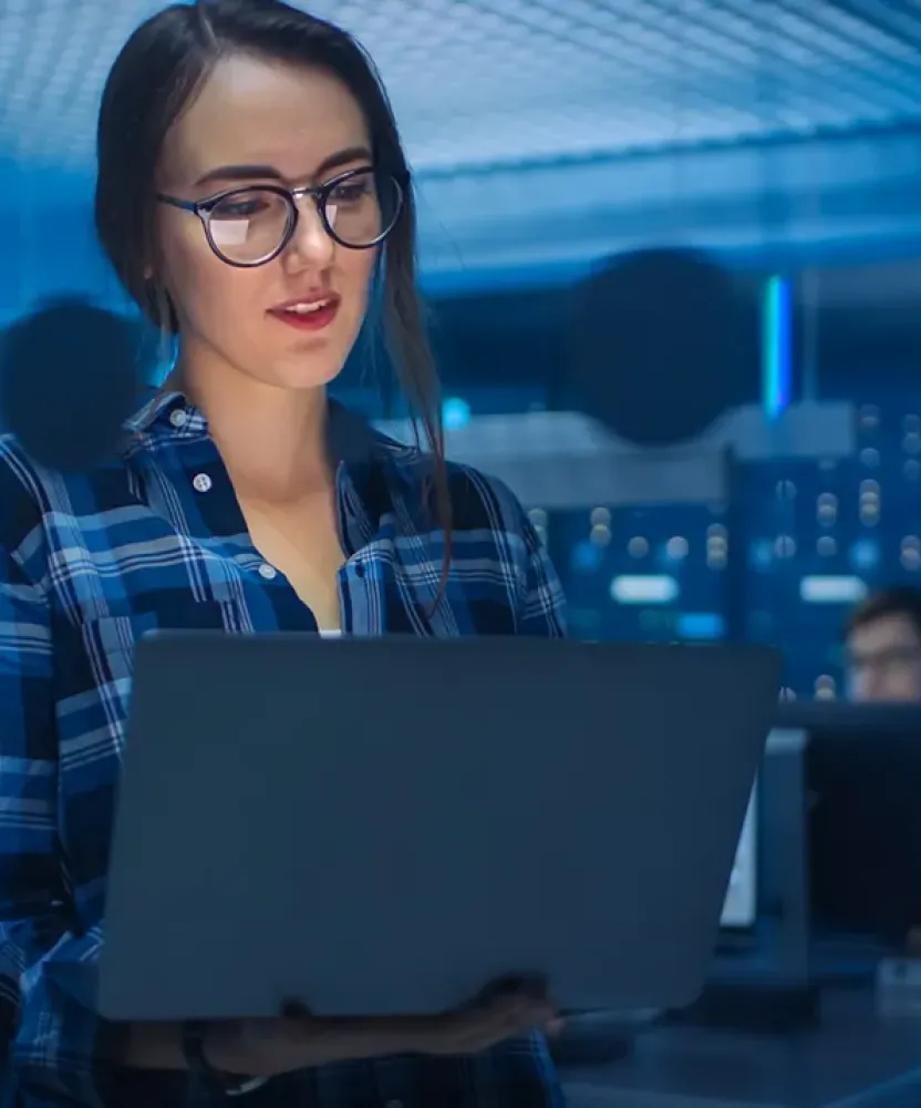 Cybersecurity analyst holding laptop in server room with coworkers in background