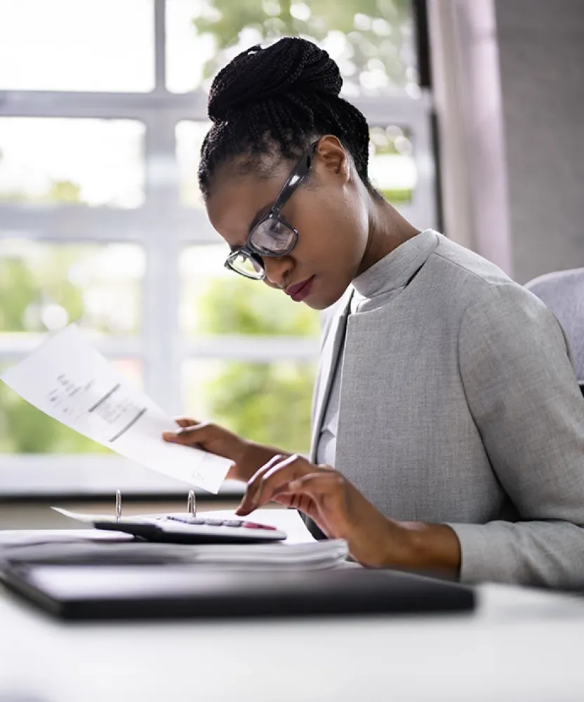 A Herzing University accounting student in professional attire reviews financial documents at a modern office desk, preparing reports and analyzing data.