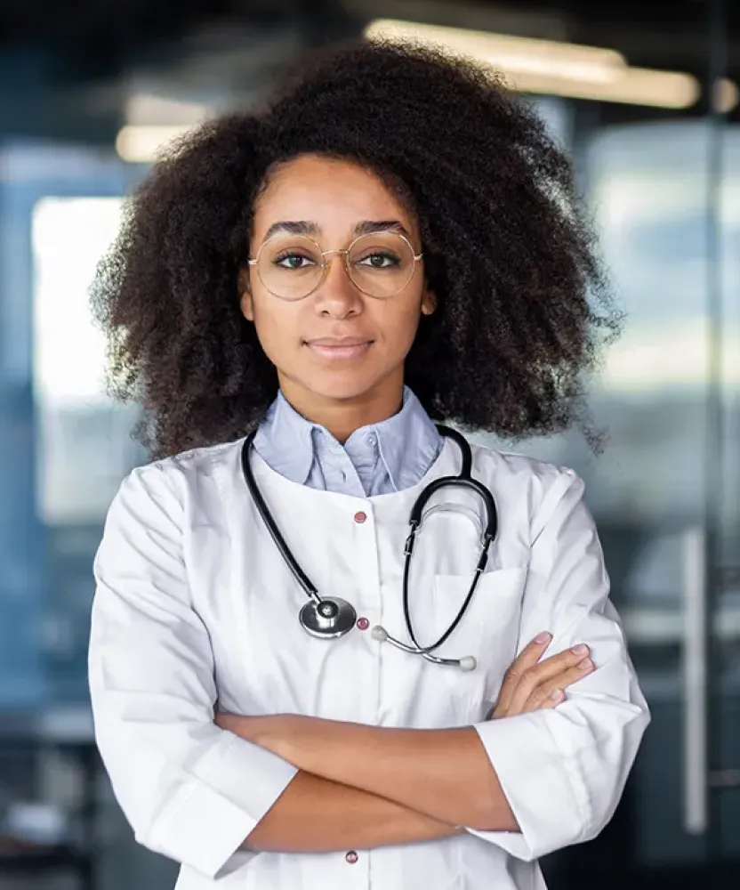 Primary care nurse practitioner student smiling with arms crossed, wearing a white coat