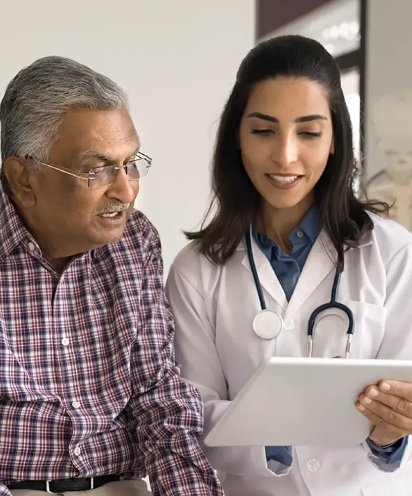 Older patient smiling while an acute care nurse practitioner reviews health information with him on a tablet