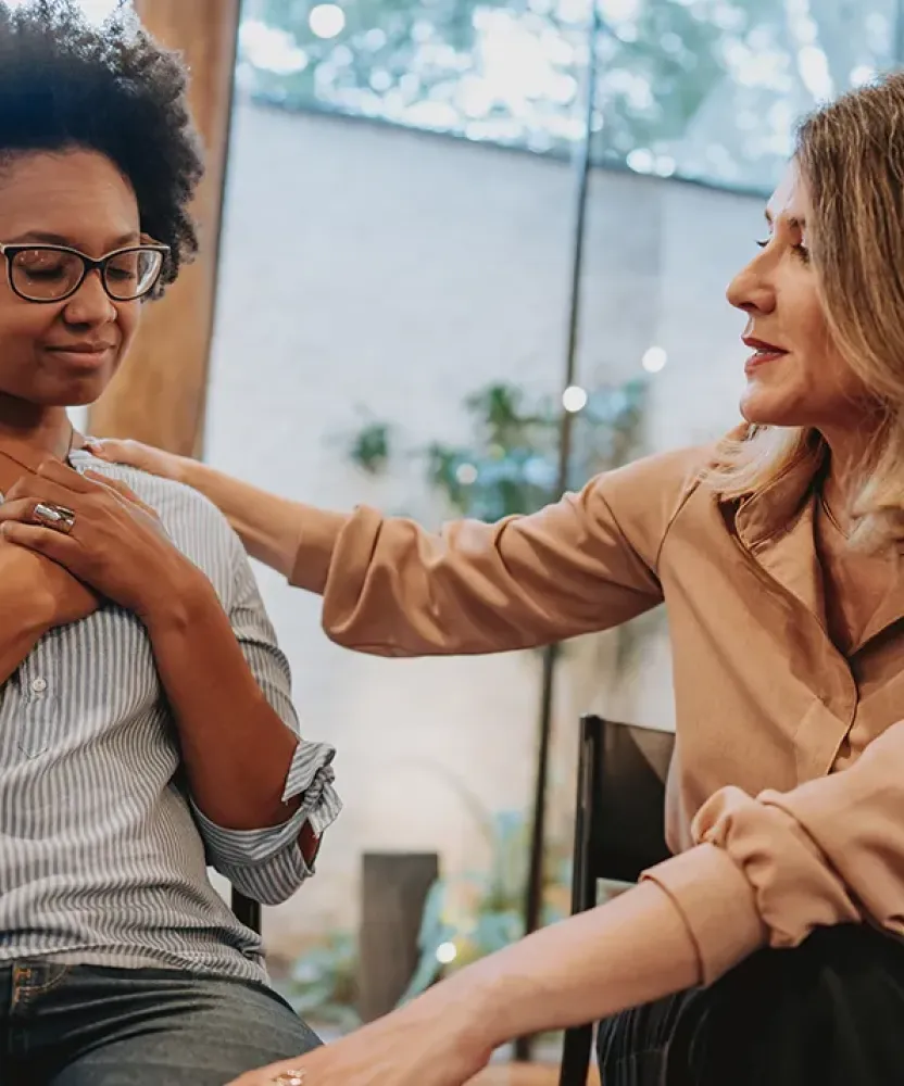 Social worker in Texas offering emotional support to a seated client, gently placing a hand on the client’s shoulder during a counseling session in a calm, private setting.