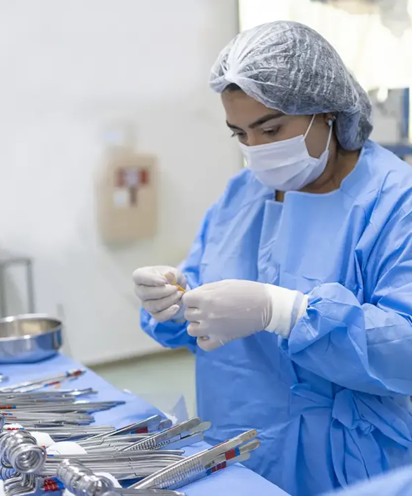 Surgical Technology student in Texas wearing protective surgical gown, mask, gloves, and hair covering prepares sterile surgical instruments in a clinical lab setting.