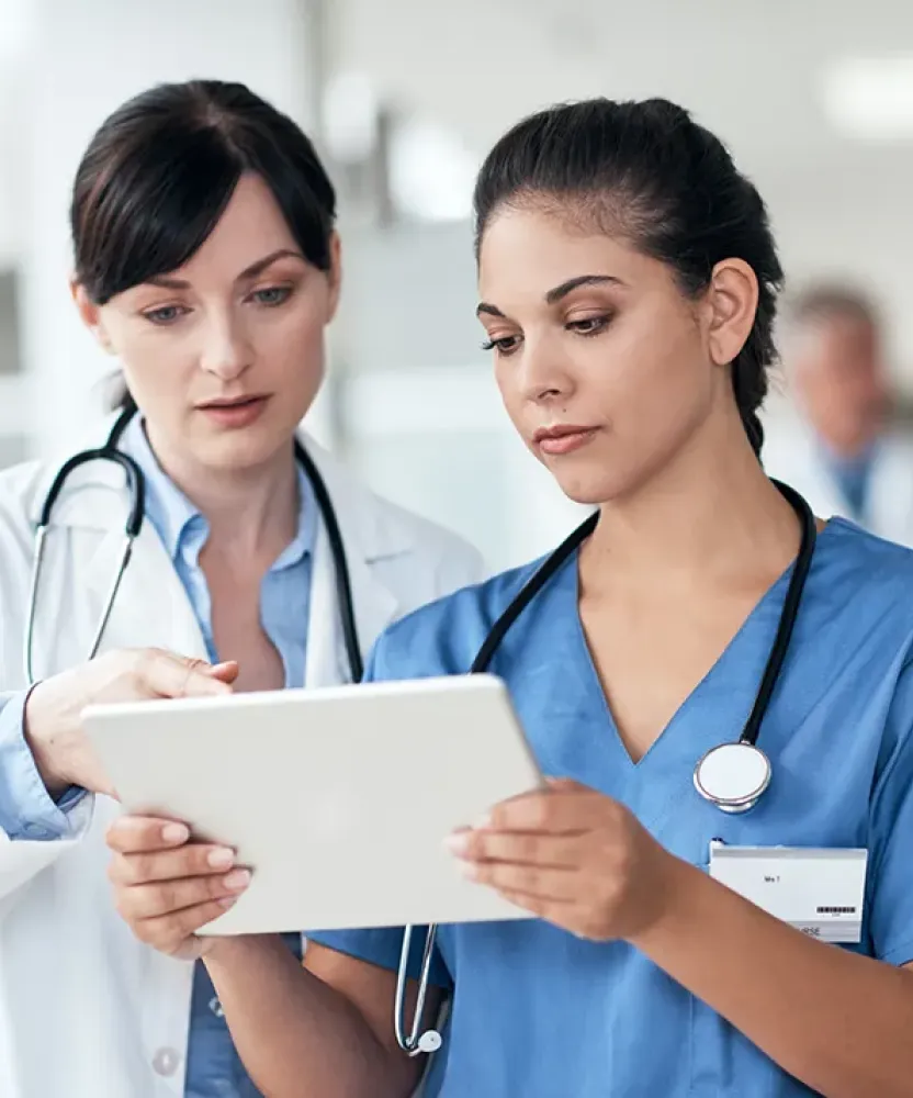 Healthcare professionals review information together on a tablet, with one clinician pointing to the screen as the other reads.
