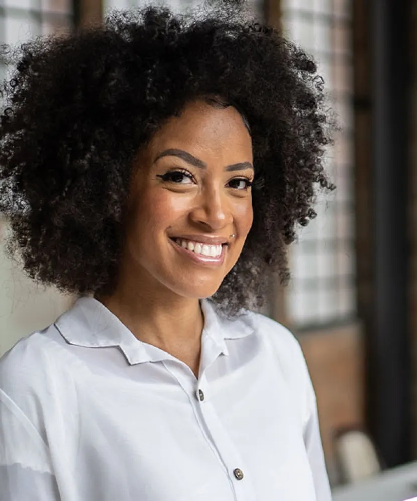 Smiling business professional holding a tablet in a modern office while coworkers collaborate around a table in the background