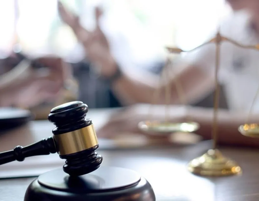 Gavel resting on desktop with scales and paralegals speaking blurred in the background