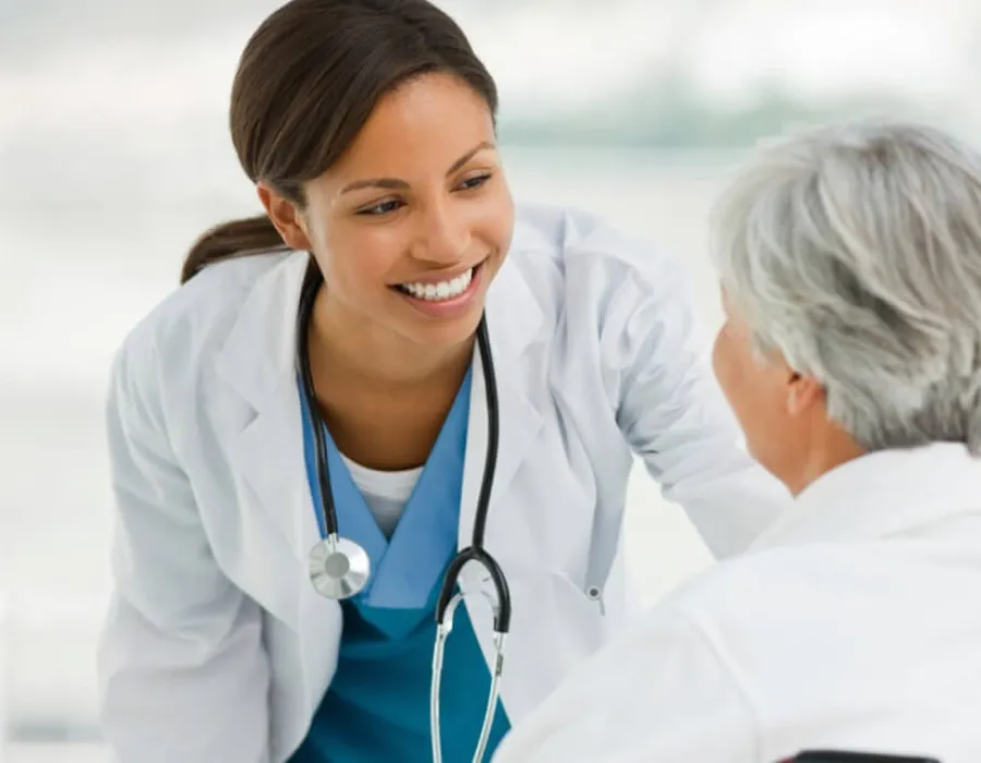 Nurse practitioner smiling while speaking with elderly patient seated in wheelchair