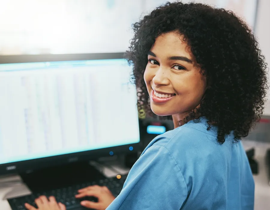 A medical billing and coding specialist smiles for the camera while working on her desktop.