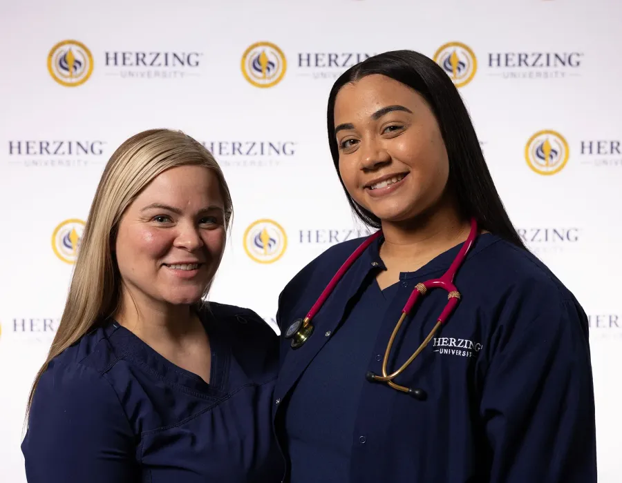 Two Herzing nursing students wearing blue scrubs smiling for photo