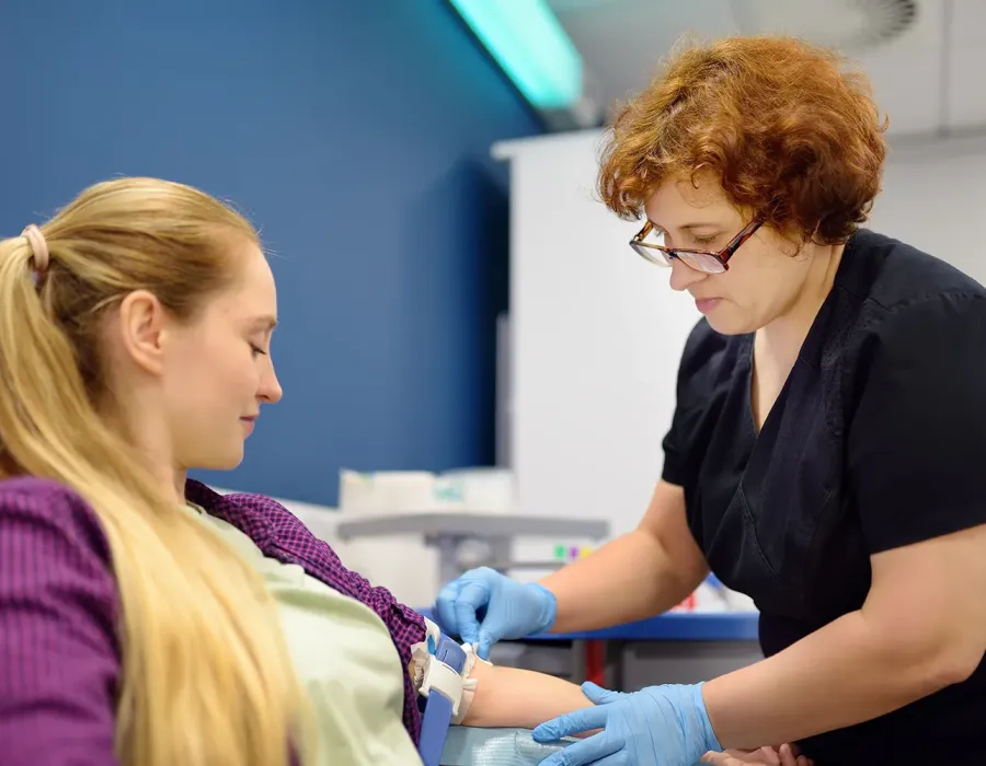 Healthcare worker drawing blood from a seated patient in a clinical setting