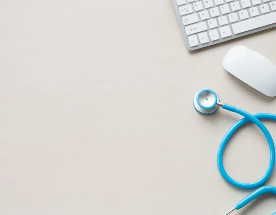 Stethoscope, mouse, and keyboard resting on desktop in well lit medical clinic