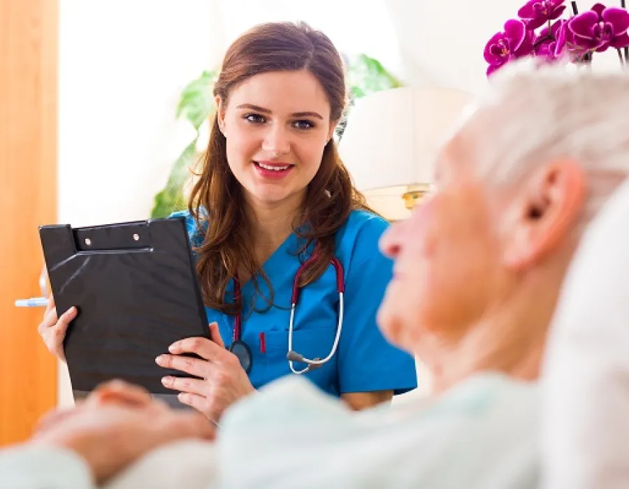 Medical assistant holding clipboard and speaking with patient in hospital room