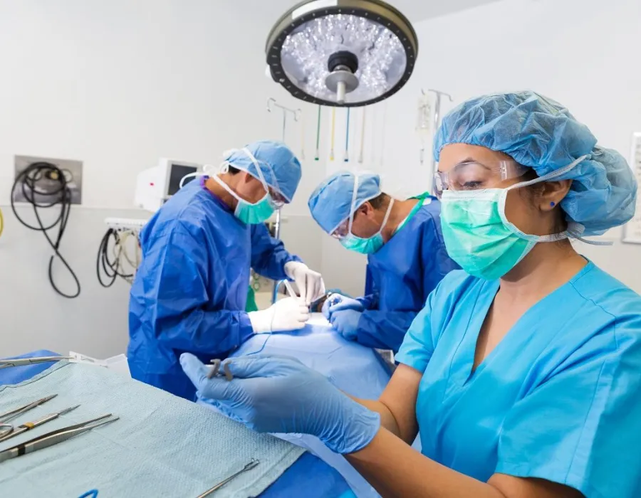 Surgical nurse handling instruments in OR while surgeons work in background