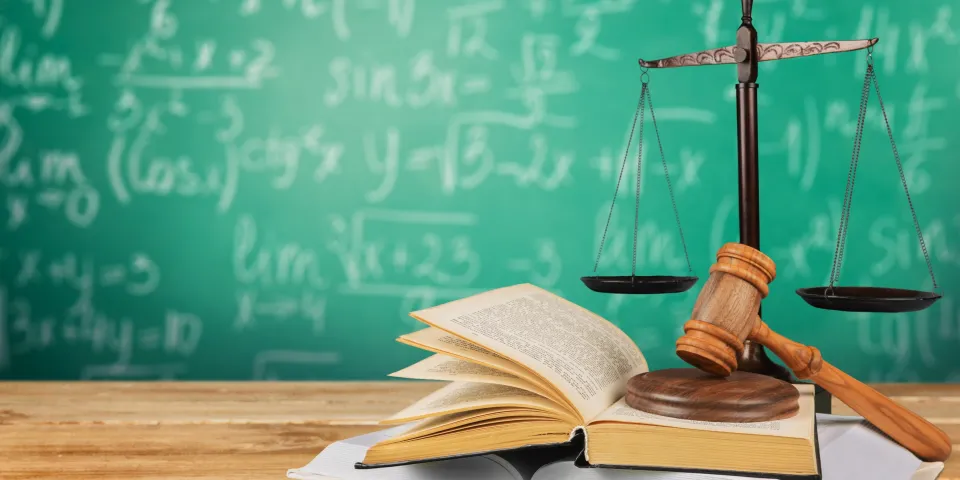 Gavel on books on a desk with scales and chalkboard in background