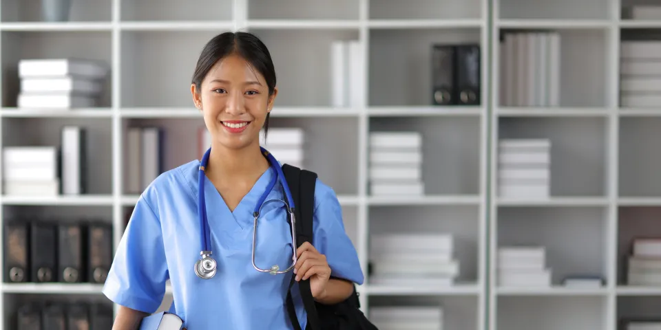Nursing student smiling in library with bag over shoulder