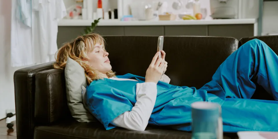 Young Caucasian nurse using smartphone while lying on black leather sofa in on call room