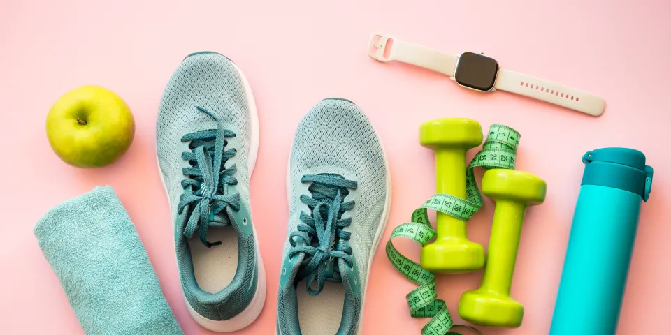 Healthy lifestyle and fitness concept. Sneakers, dumbbells, towel, green apple and fitness bracelet.
