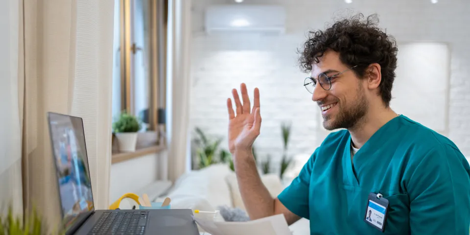 A young Caucasian male nurse in scrubs, having a video call while working from his home