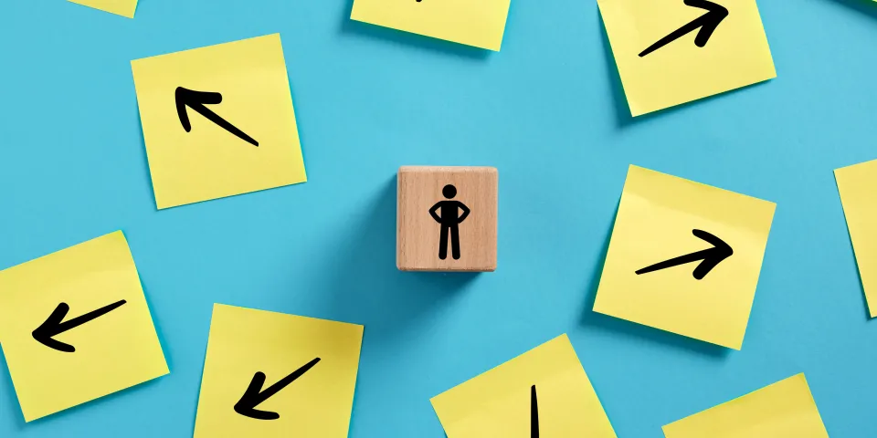 Decision making in business. Choosing a path to follow. Businessman standing on a wooden block, surrounded by arrows pointing in various directions.