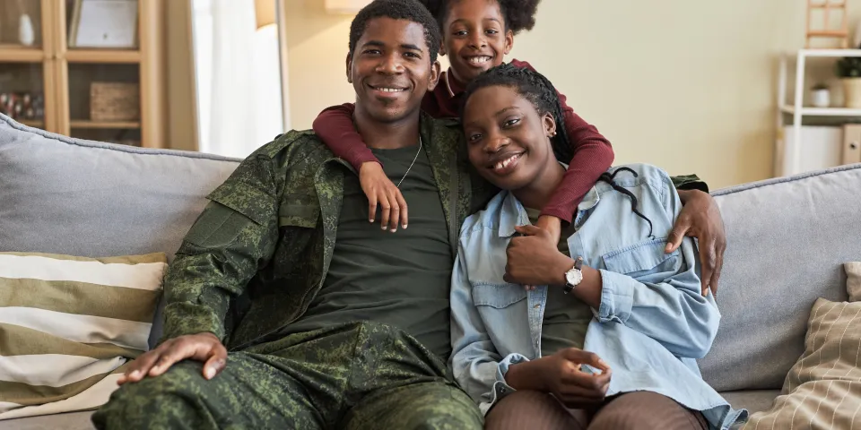Portrait of African American family of three smiling at camera sitting on sofa with their military dad
