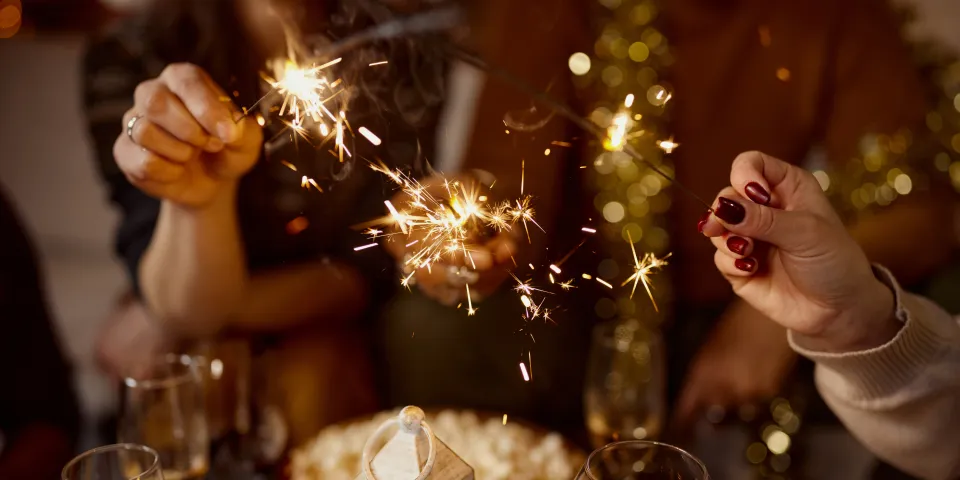 Close up of unrecognizable friends having fun with sparklers while celebrating Christmas at home.