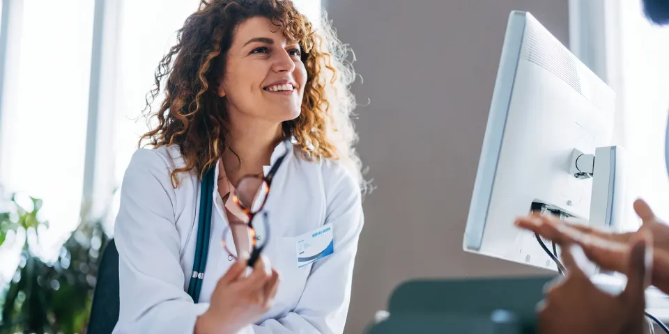 A smiling nurse in a white coat speaks with a patient during a consultation in a bright medical office.