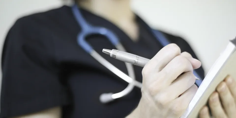 Health professional wearing stethoscope writing on pad of paper
