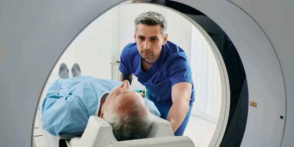 Radiologic technologist positions an older patient on the table of a CT scanner, preparing them for a medical imaging exam.