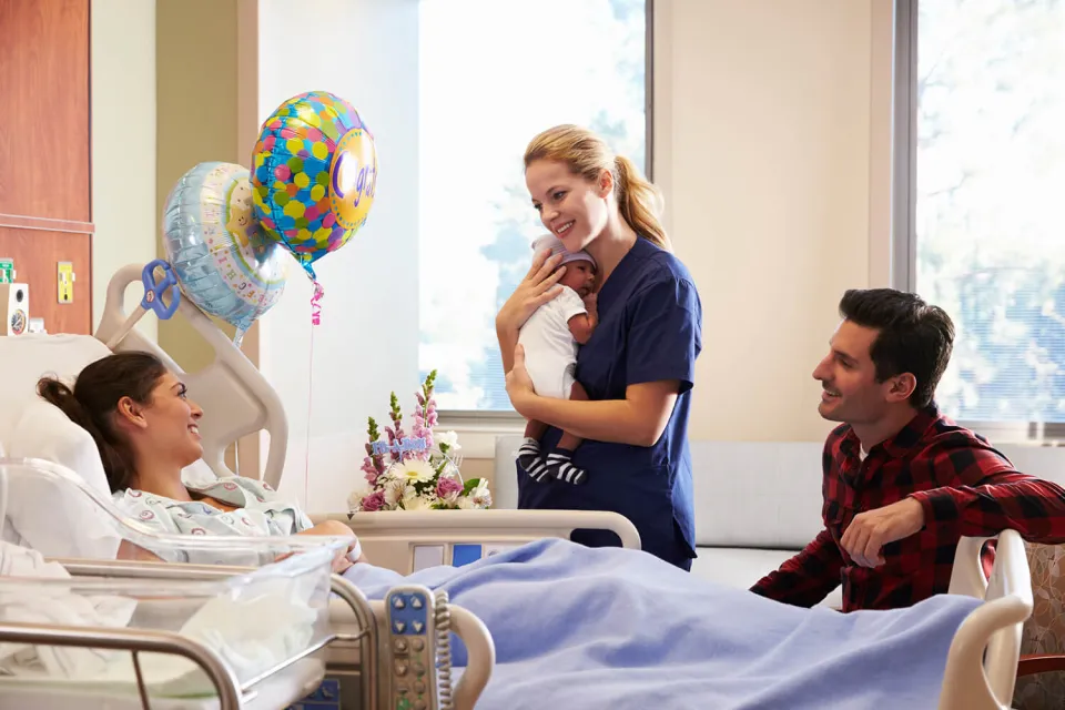 Labor and Delivery Nurse Holding Infant and Smiling with New Parents