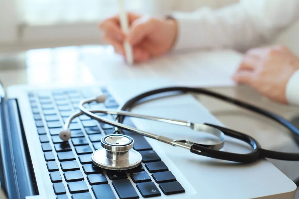 Health Information Management Professional Taking Notes by Laptop with Stethoscope